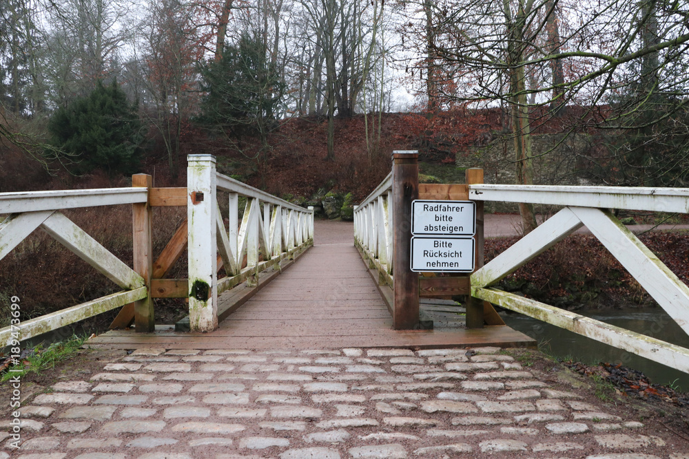 old german bridge in park with warning sign for bicyclist: Please dismount and take care.