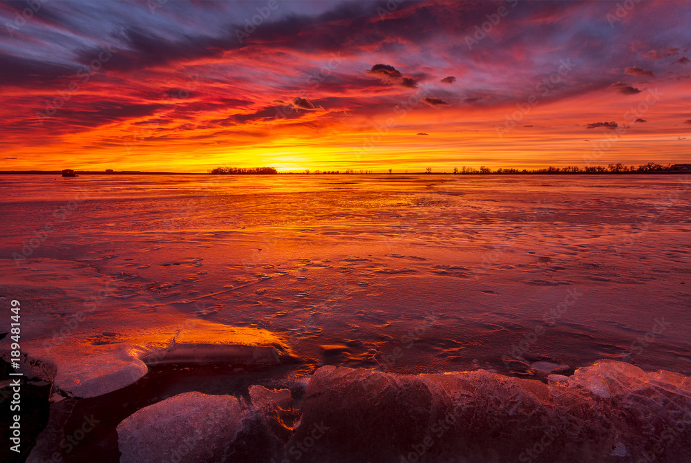 Colorful Sunrise or Sunset on a frozen lake with rocks in the foreground