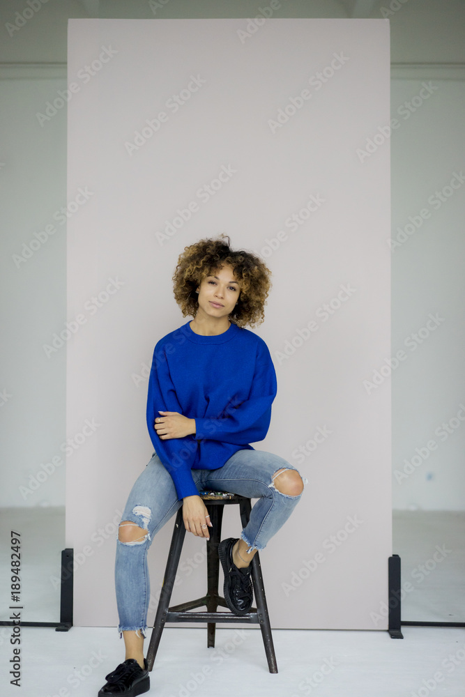 Portrait of serious woman wearing blue pullover sitting on stool Portrait of serious woman wearing blue pullover sitting on stool