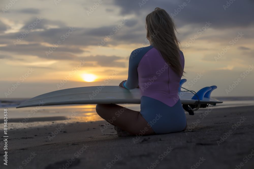 Indonesia, Bali, young woman with surfboard sitting on beach at sunset