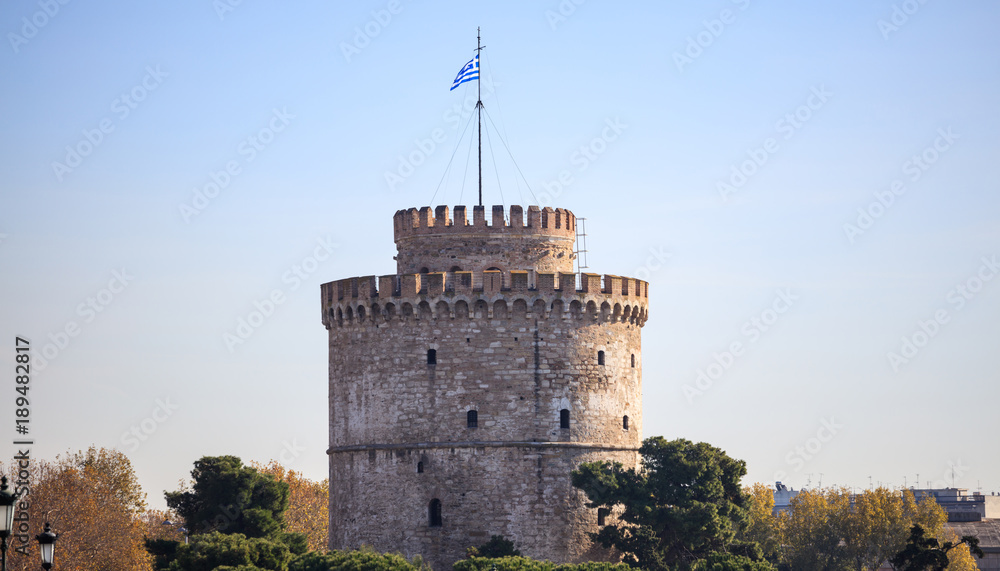 The White Tower in Thessaloniki, Greece. Trees around it. Clear blue sky background.