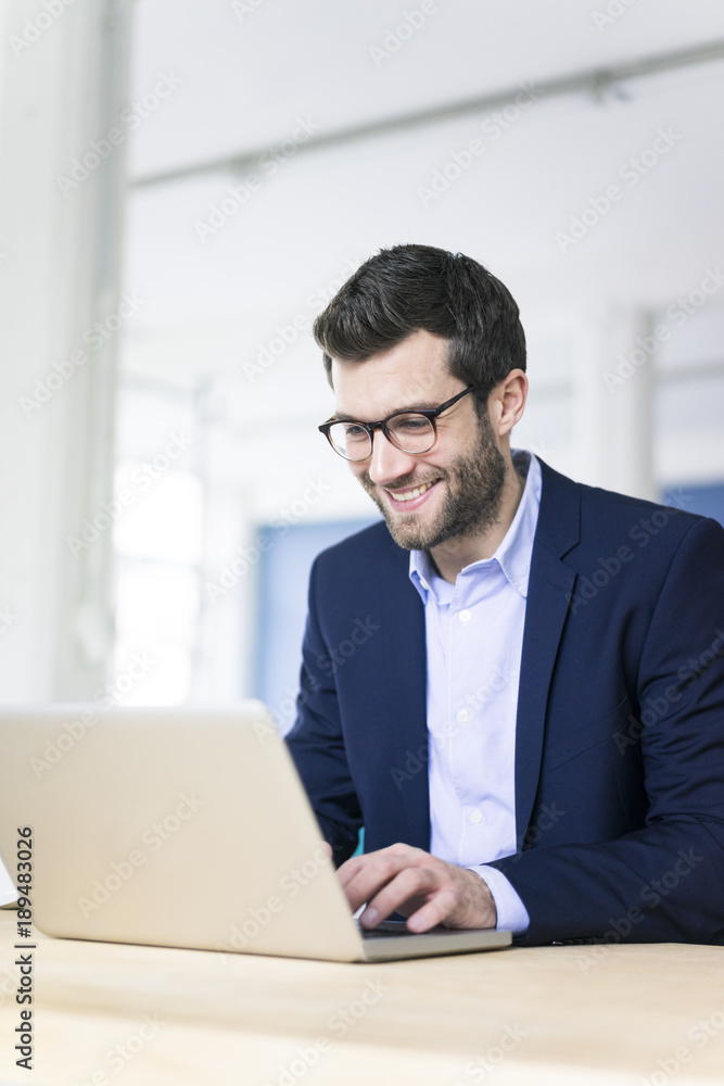 Smiling businessman using laptop on desk in office Smiling businessman using laptop on desk in office