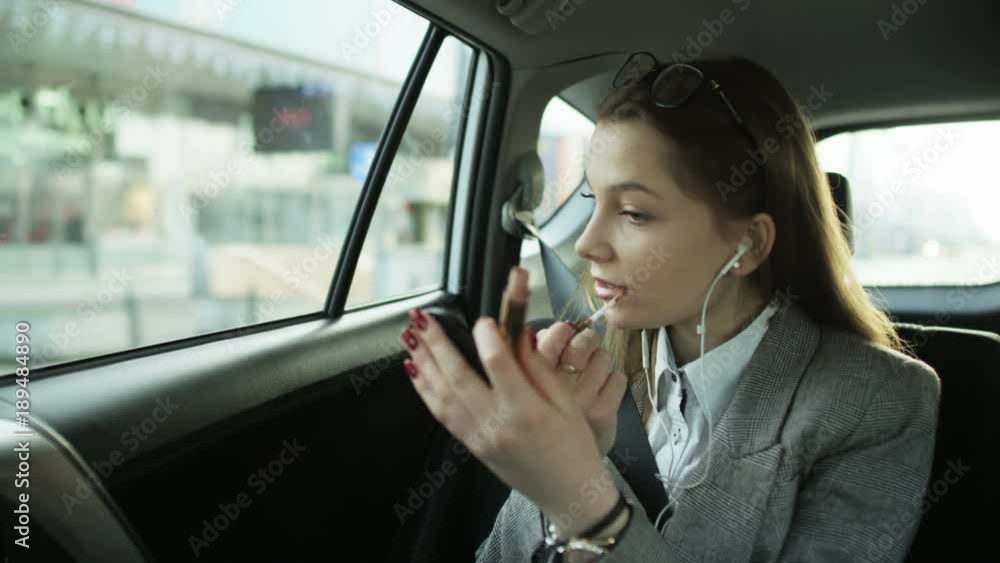 Businesswoman Putting on Lip Gloss in the Moving Car Businesswoman Putting on Lip Gloss in the Moving Car