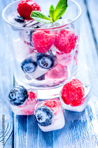 glass with frozen berries in cubes on wooden desk background