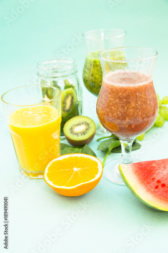 Preparing homemade tropical smoothie with kiwi, grapes, banana, orange, watermelon and spinach on a light blue background. Diet, Fitness, Dessert Concept