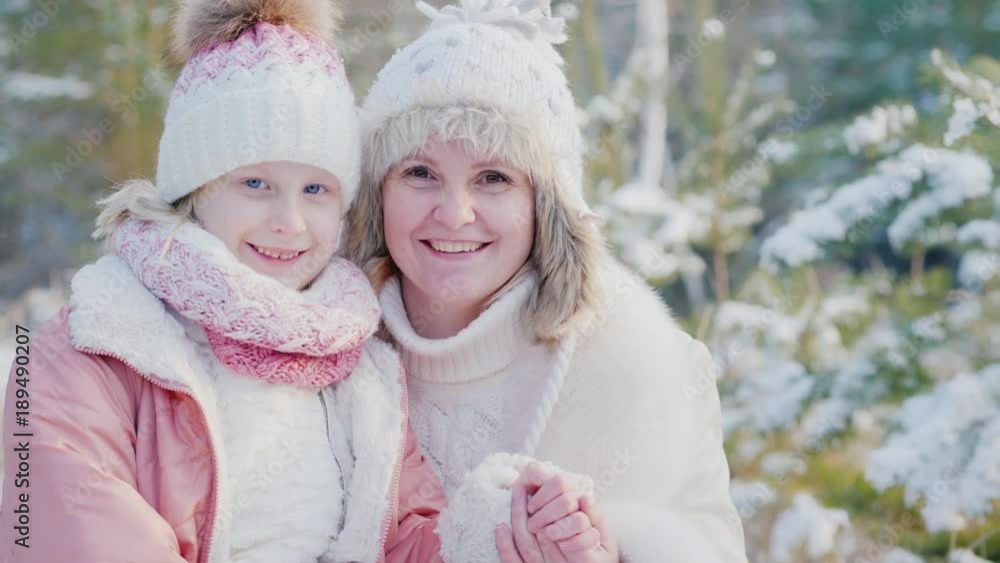 Winter portraits of mother and daughter. Smiling, looking at camera against the background of snow-covered forest Winter portraits of mother and daughter. Smiling, looking at camera against the background of snow-covered forest