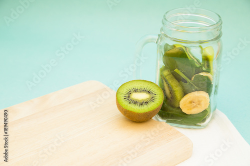 Preparing green smoothie. A glass jar with ingridients: kiwi, banana and spinach on a wooden cutting board, light blue background. Diet, Fitness, Dessert Concept