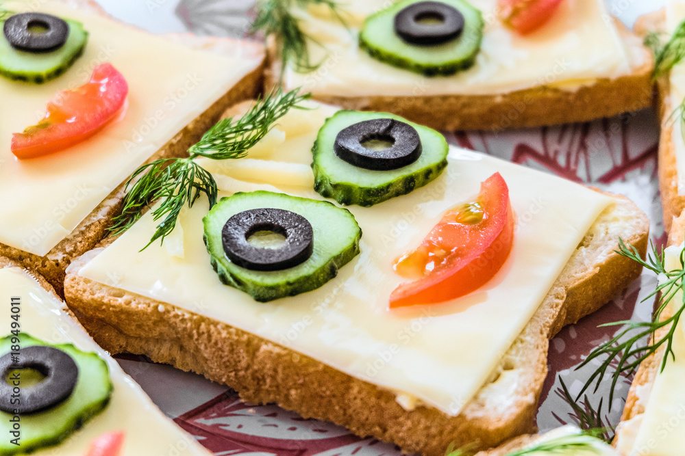 Smiling cheese sandwich with face from cucumbers, tomato, olives and dill. Perspective view.