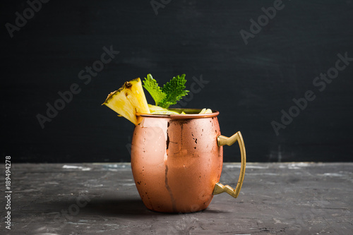 Photography Cold pineapple Moscow Mule cocktail in copper mug on the rustic background