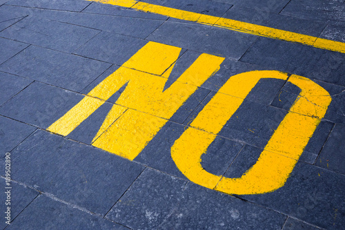 the word "no" painted in yellow on gray asphalt