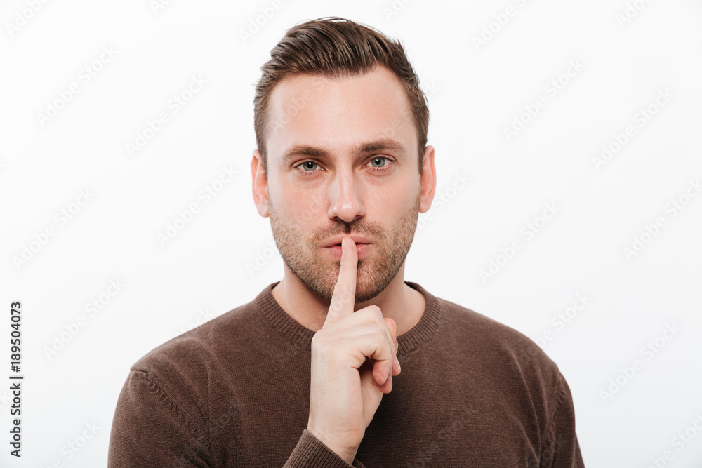 Handsome young serious man showing silence gesture Handsome young serious man showing silence gesture