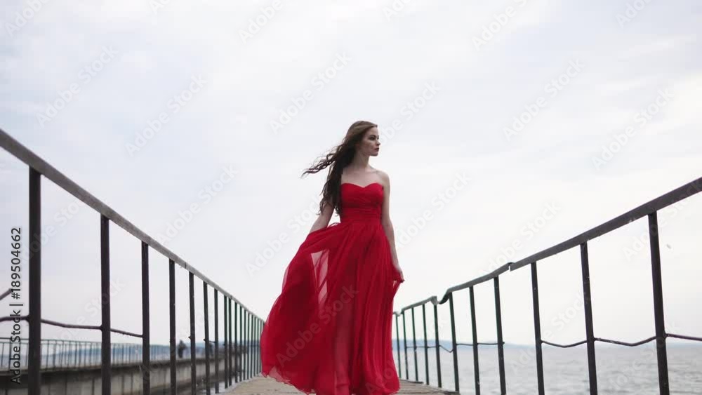a young woman who is dressed in a red dress is standing next to the sea ...