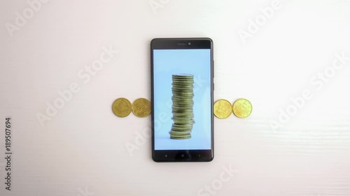 Smartphone and gold coins on white table. Slow motion animation. Ultra HD 4K video photo