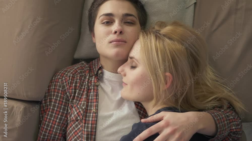 Two young lesbian girls lie on the couch, hug, cuddle, sleep, girl with short hair looks at the camera, lgbt family concept, top shot 60 fps Stock ビデオ | Adobe Stock