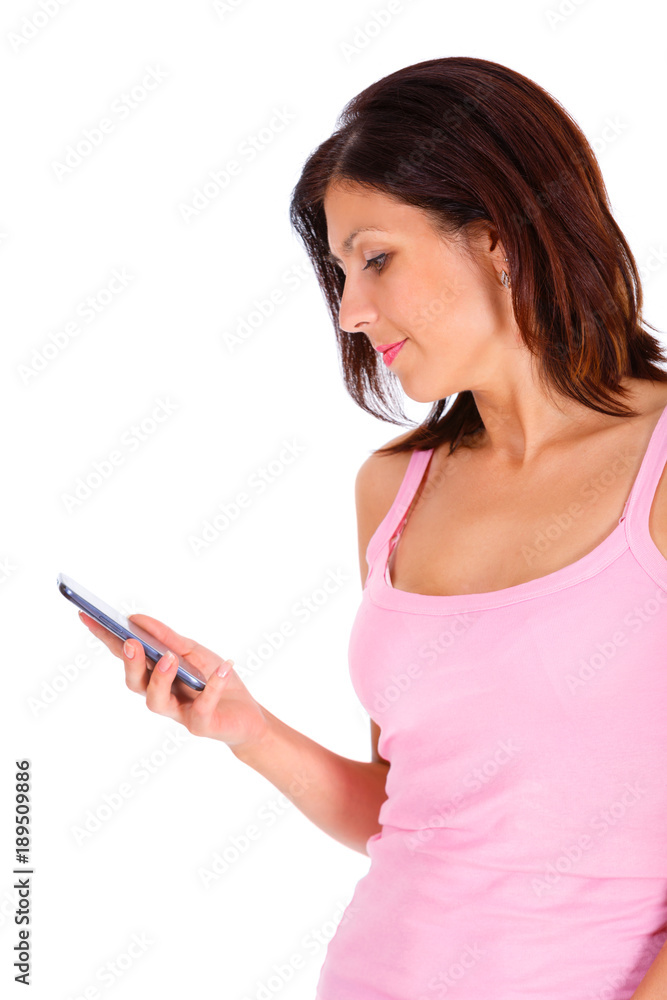 Portrait of slim brunette tanned woman with short hairstyle, dressed in t-shirt pink color and turquoise jeans, read and write sms by cell mobile phone. Isolated on white background. Positive emotion Portrait of slim brunette tanned woman with short hairstyle, dressed in t-shirt pink color and turquoise jeans, read and write sms by cell mobile phone. Isolated on white background. Positive emotion