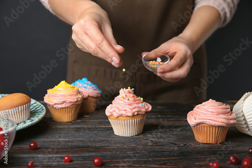 Female baker decorating tasty cupcake with sprinkles at table