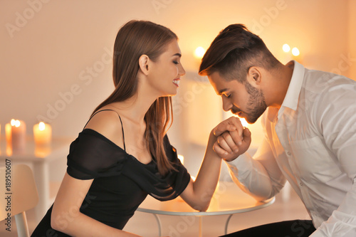 Young man kissing his girlfriend's hand in room with burning candles