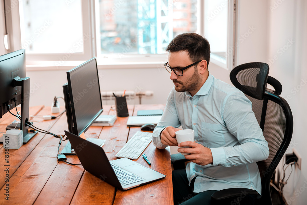 Young handsome businessman at his laptop working in modern office. Young handsome businessman at his laptop working in modern office.