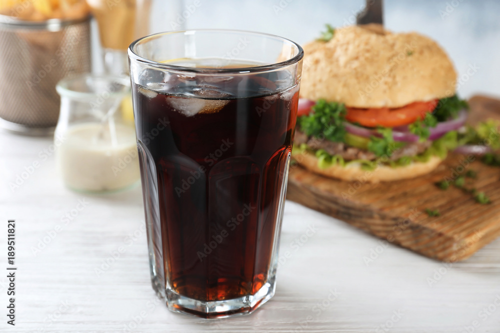 Glass of cold cola with tasty burger on table Glass of cold cola with tasty burger on table