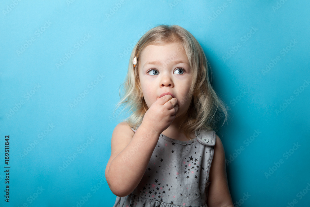 A little girl is isolated on a blue background eating a sweet candy. A little girl is isolated on a blue background eating a sweet candy.