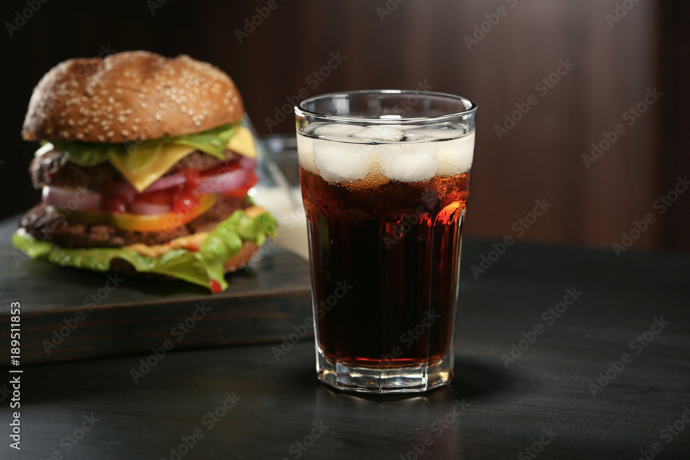 Glass of cold cola with tasty burger on dark background Glass of cold cola with tasty burger on dark background
