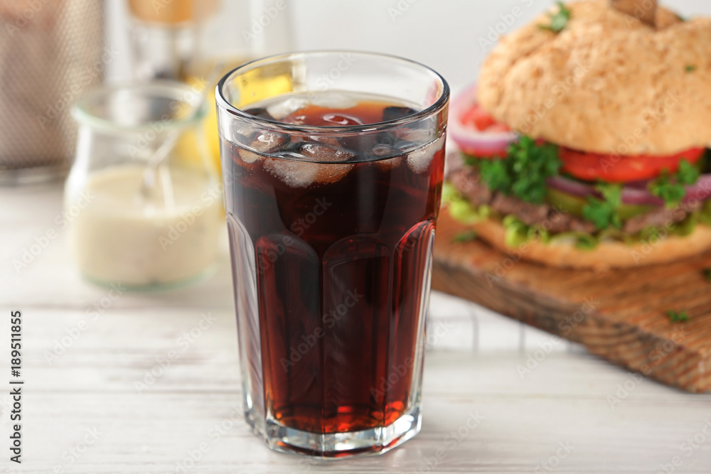 Glass of cold cola with tasty burger on table Glass of cold cola with tasty burger on table