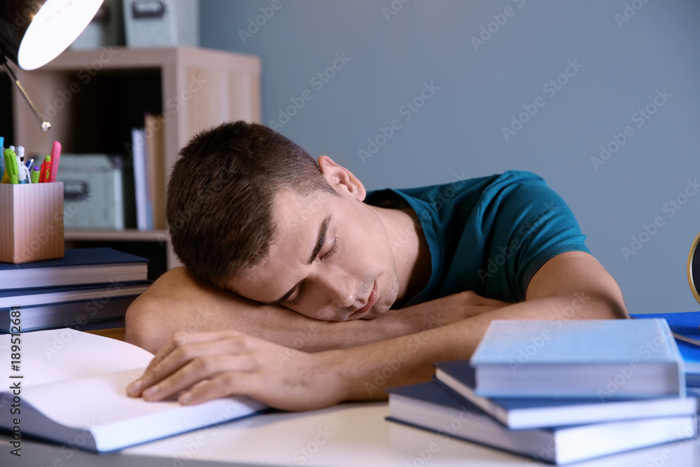 Tired student sleeping at his desk indoors. Preparing for exam Tired student sleeping at his desk indoors. Preparing for exam