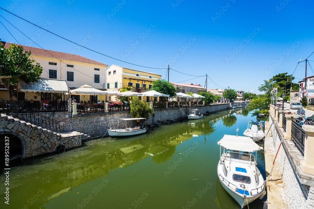 Small local river at center of small town with cafe, bar and restaurant on the waterfront and parked boats in Corfu, Greece.