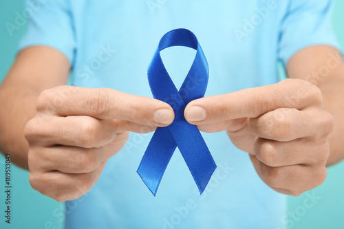 Man holding blue ribbon on color background, closeup. Prostate cancer awareness