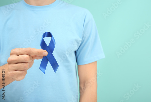 Man holding blue ribbon on color background, closeup. Prostate cancer awareness