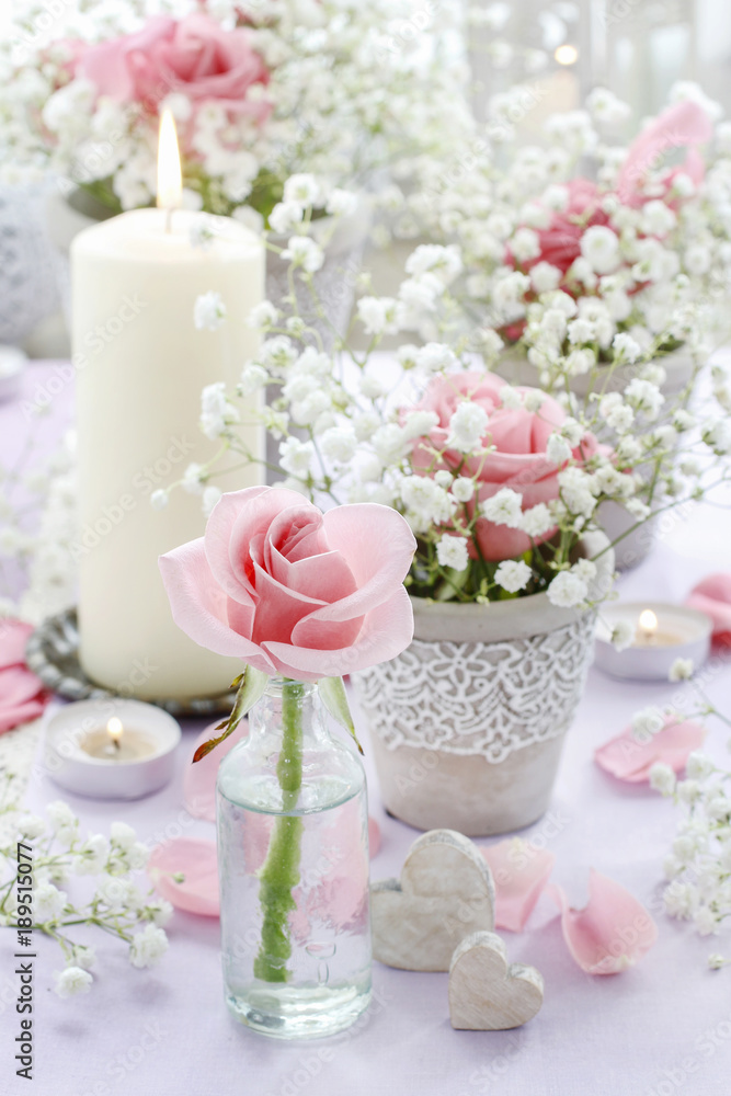 Floral arrangement with pink roses, gypsophila paniculata and candles.