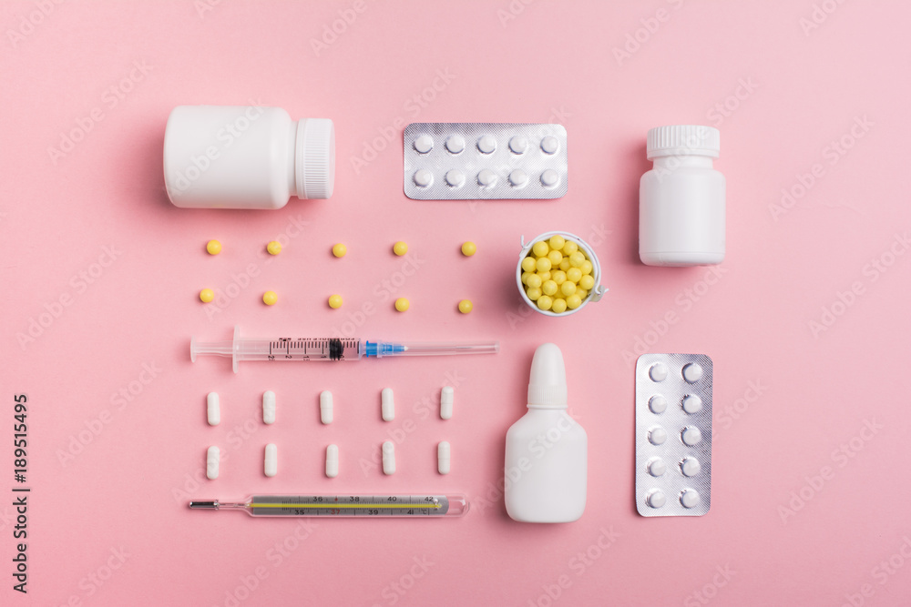 Illness concept: tablets and a thermometer on a pink background top view Illness concept: tablets and a thermometer on a pink background top view