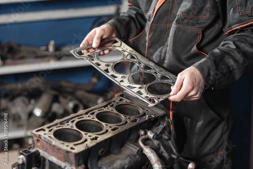 Sealing gasket in hand. The mechanic disassemble block engine vehicle. Engine on a repair stand with piston and connecting rod of automotive technology. Interior of a car repair shop. photo