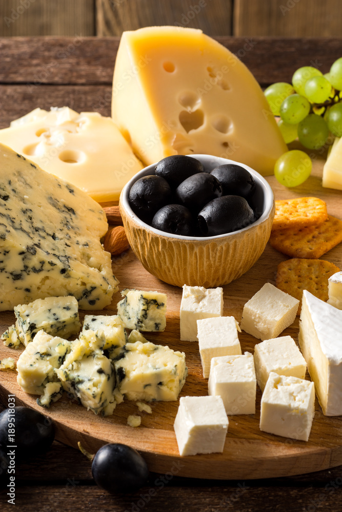Various types of cheese on wooden cutting board.