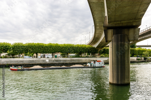 A dry bulk cargo barge loaded with gravel heading up the river Marne in the suburbs of Paris, passing under the ramps of the A86 highway. photo