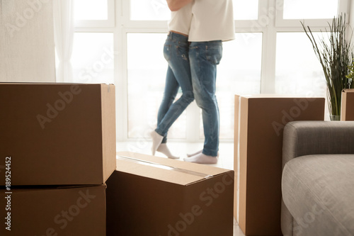 Moving boxes with couple embracing at background, boyfriend and girlfriend starting new life in own bought rental apartment, homeowners packed belongings to move ready for relocation, close up view © fizkes