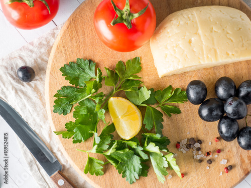 Piece of cheese with parsley, tomatoes grapes on a cutting Board with a knife