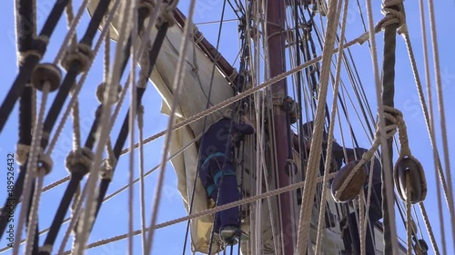sailors climb up the mast on a rope ladder on a traditional sailing ship.