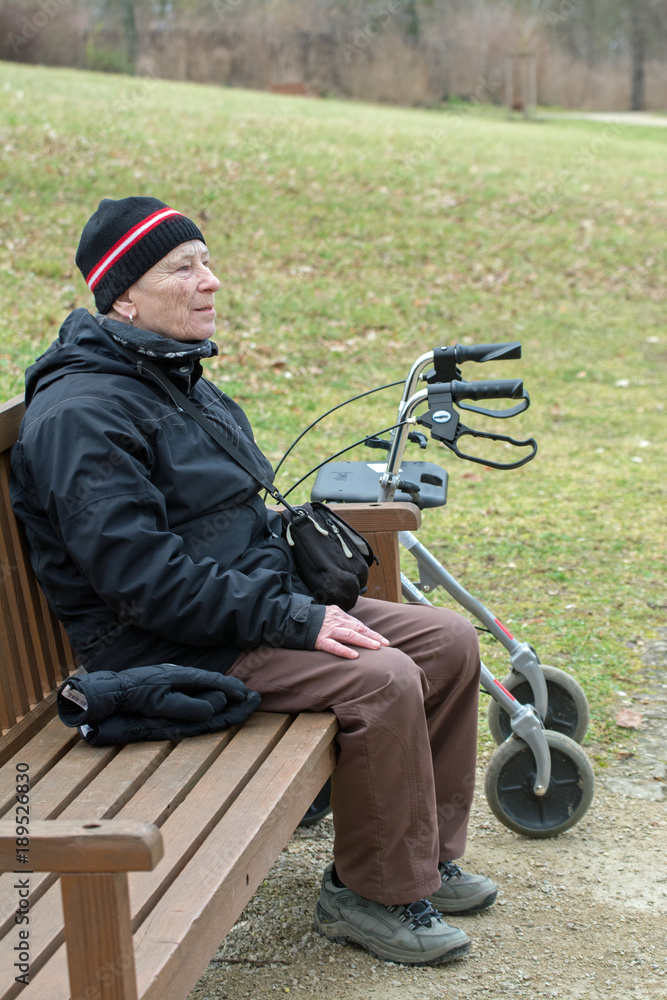 seniorin neben rollator sitzt auf einer parkbank