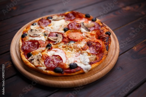 Freshly baked pepperoni pizza with mushrooms on the wooden plate, shallow depth of field