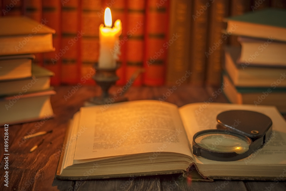 Fototapeta premium On the wooden background of the table there are stacks of colorful books near the old candlestick with burnt matches lying next to each other.