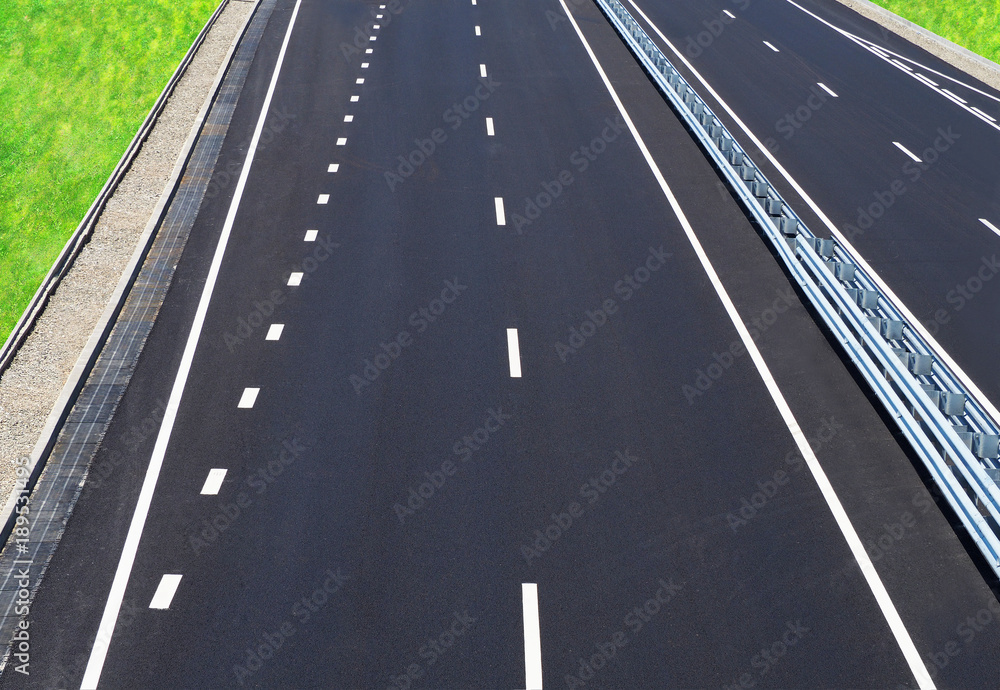 Asphalted highway. Empty motorway. High-speed road of the city. Barrier, guarding rail. Perspective, convergence, top view. Rainwater drainage system, runoff, green grass on the roadside Asphalted highway. Empty motorway. High-speed road of the city. Barrier, guarding rail. Perspective, convergence, top view. Rainwater drainage system, runoff, green grass on the roadside