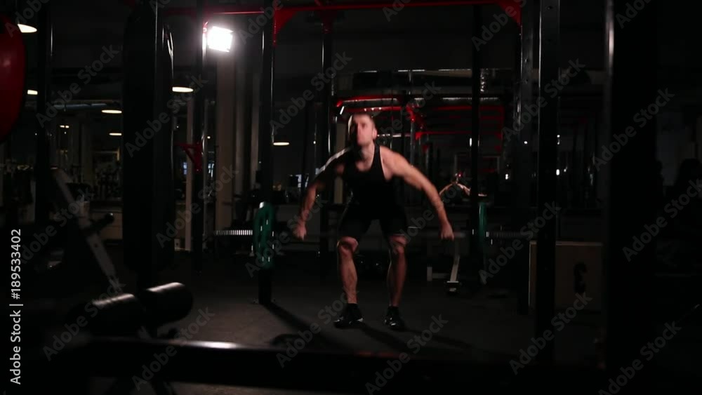 A sports athlete in the gym raises the bar with a weight above his head from the sitting position. A sports athlete in the gym raises the bar with a weight above his head from the sitting position.
