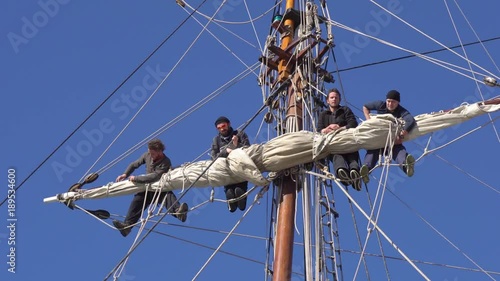 Sailors work with sails at a height on a traditional sailboat