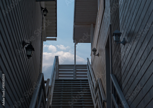 Two houses stand side by side, balconies, stairs, roofs, against a blue sky with clouds, cloudy day, steps, downspouts