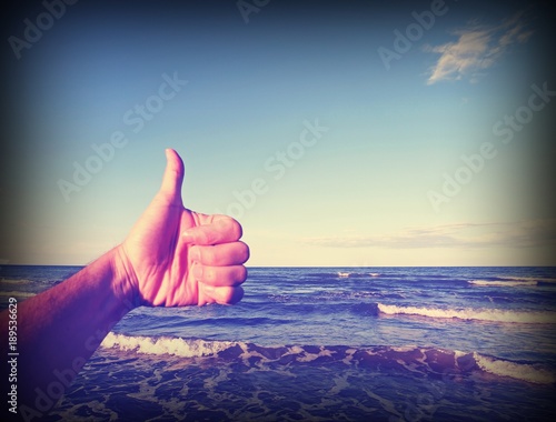 thumb up to indicate ok next to the sea with vintage old effect photo