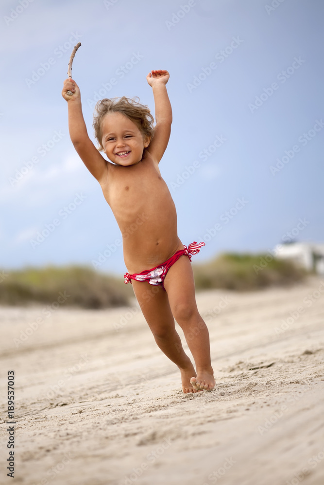 Jumping Baby Girl on the beach with a stick Stock Photo