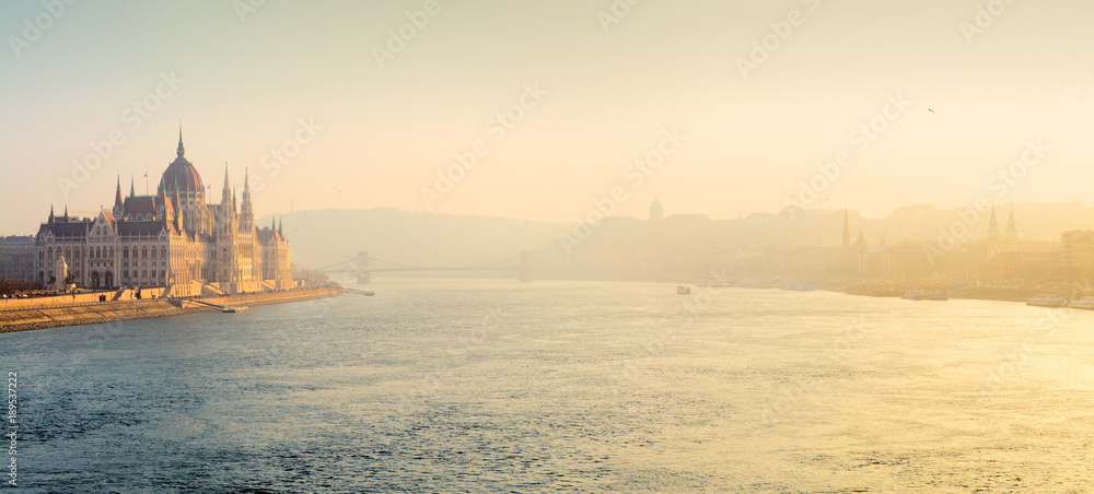 Panoramic view of sunlit Danube river with Parliament building in mist