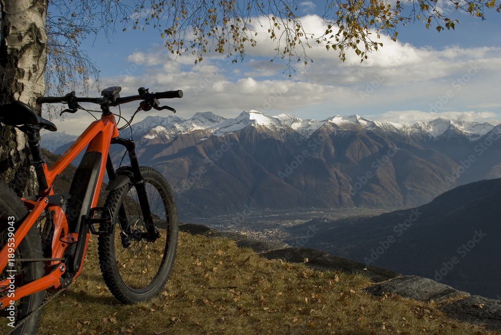 ebike, e-bike, electric bicycle, high mountain, leaning against a tree, detail of handlebars, wheels, saddle, display, alps landscape, snow covered tops, autumn, Antrona Valley, Piedmont, Italy ebike, e-bike, electric bicycle, high mountain, leaning against a tree, detail of handlebars, wheels, saddle, display, alps landscape, snow covered tops, autumn, Antrona Valley, Piedmont, Italy