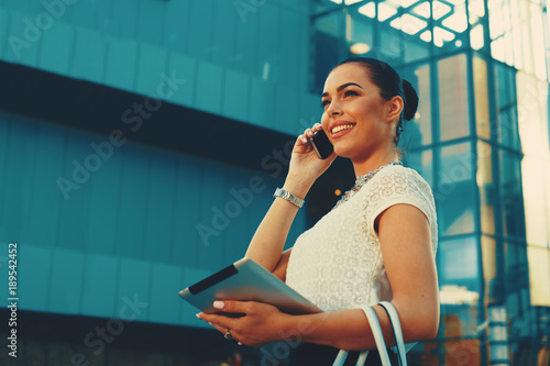 Young businesswoman talking on the phone with digital tablet in hand outdoor